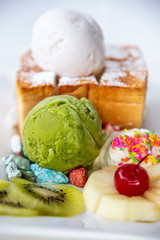 Closeup Honey Toast bread served with green tea and coconut milk ice cream scoop, decorate with cherry, apple, kiwi fruit, and cream sugar topping sprinkle on a white dish sweet cool snack in summer