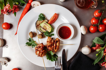 Barbecued marinated turkey or chicken meat shish kebab skewers with ketchup sauce and grilled vegetables on rustic wooden table background. Traditional barbecue grill food
