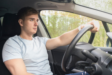 Handsome serious guy, driver, young concentrated focused on road man driving a car, holding...