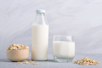 oat milk, gluten-free vegetarian organic milk, a glass bottle and a glass of oat milk on a gray background