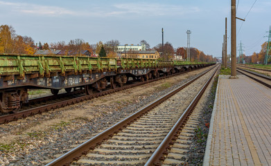 Fototapeta na wymiar Landscape with railroad track and chain of old rusty green cargo wagons standing near platform.