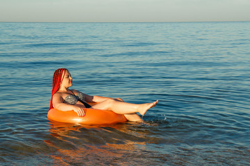 A young woman with African pigtails is sunbathing in an rubber ring in the sea near the shore.