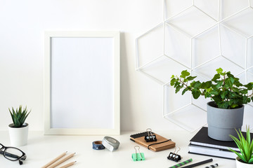 Desk with office supplies and a white frame mockup. Blank wall copy space.