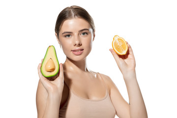 Portrait of beautiful young woman with avocado and orange over white background. Concept of cosmetics, makeup, natural and eco treatment, skin care. Shiny and healthy skin, fashion, healthcare.