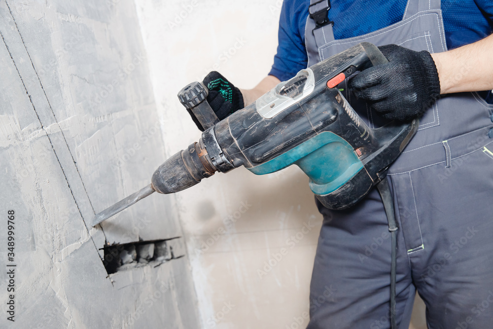 Wall mural builder worker man with hammer drill perforator equipment making hole in gray wall construction