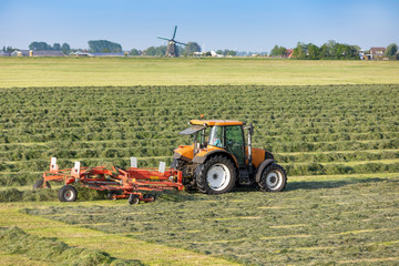 Obraz premium A tractor with a mower in Sassenheim. On the background the historic Lisserpoel windmill. On the Rooversbroekdijk in the Hellegatspolder in the Netherlands.