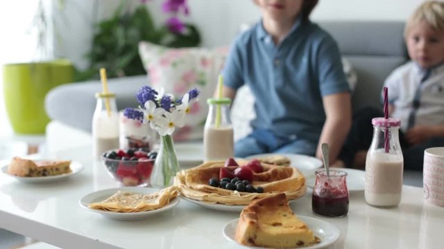 Happy family, having pancakes for breakfast, eating in living room, talking and laughing, cozy home