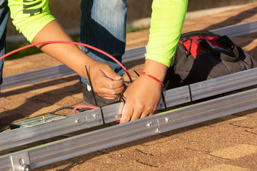 An electrical technician attaches a red wire to the framework that will hold solar panels with zip...