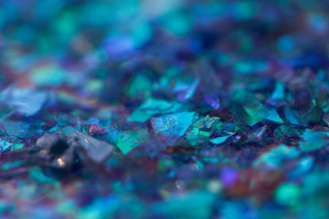 Macro photo of small rainbow glossy pieces of decorative foil in blue shades.