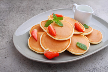 Pancake in a plate with strawberries decorated with mint on a concrete background