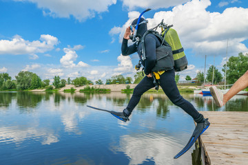 Scuba diver with equipment and flippers jumps in water from pier after boot kick