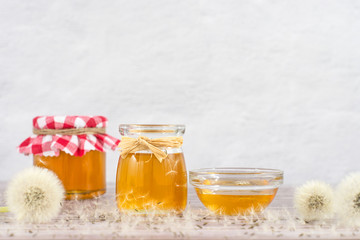 Dandelion jam, honey, jelly in a glass jar on a wooden table, white background with fresh flowers, dandelion airy seed heads, seeds, blow balls. Medicine, healthy food, health benefits from nature