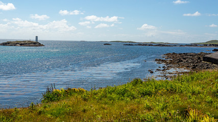 Rocky coastal meadow with green grass, the lighthouse on Gun Rock and the Atlantic Ocean in the background, sunny spring day on Inishbofin Island, County Galway, Ireland