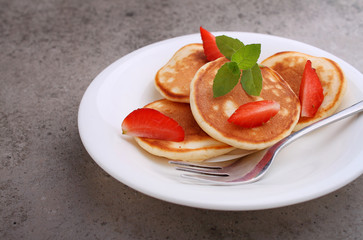 Pancake in a plate with strawberries decorated with mint on a concrete background