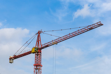 Red tower crane against light blue sky with white clouds. Close up. Copy space.