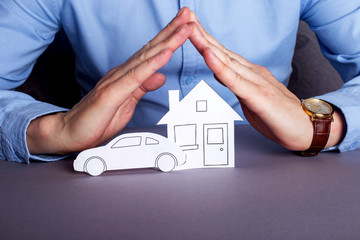 Insurance for the car and the house. Man in a shirt covers his hands with his house and car