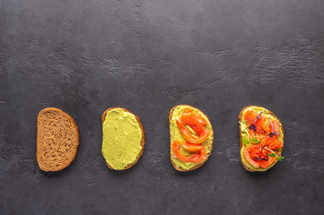 Stages of making a sandwich of bread, guacamole, salted salmon, baked tomatoes and greens