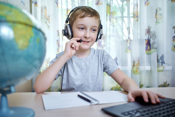 Boy in headphones talking through a laptop while doing homework at home