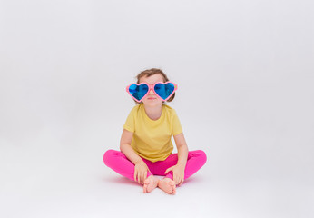 Cute funny girl sitting in big funny glasses on a white background place for text. A blonde girl in a yellow t-shirt and pink leggings. Day of laughter