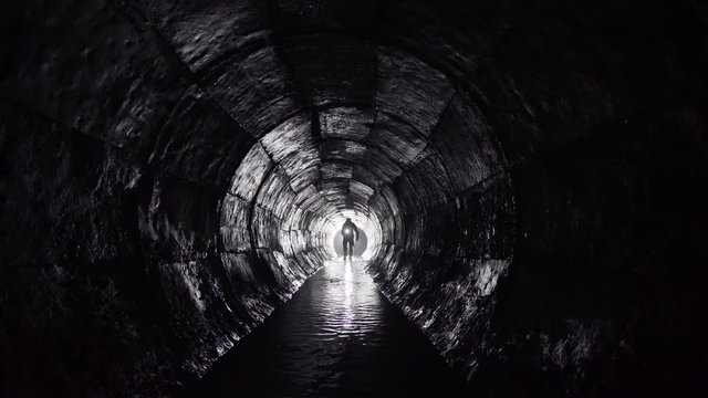 A man with a lantern walks in an underground round concrete rain collector.