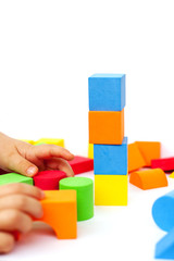 A child builds a pyramid of cubes on a white background. The boy's hand holds a cube.