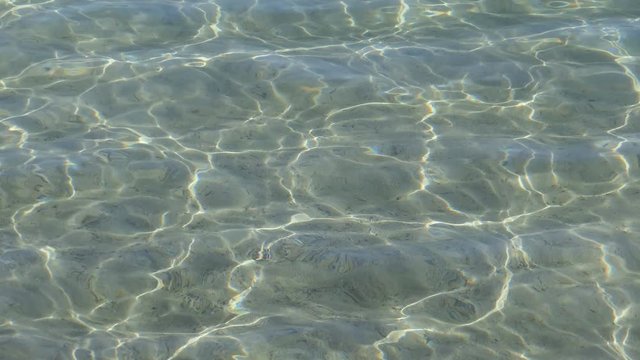A view of the sea's sandy bed from crystal clear water.
