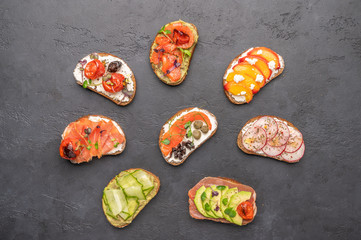 Homemade sandwiches with bread and various ingredients and spices on a dark background. Healthy delicious food for breakfast and lunch