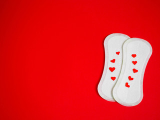 two white sanitary pads top view with red hearts on a red background. feminine hygiene