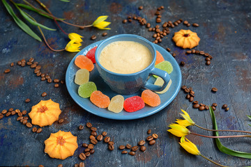 Obraz na płótnie Canvas View of bright fruit marmalades on a blue plate, a cup of coffee with thick foam, cookies and yellow tulips on a dark background. Healthy desserts