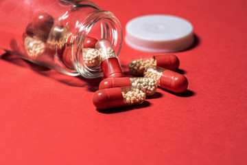 Red pills with white granules fell out of a glass jar on a red background. Medicinal capsules, tablets.