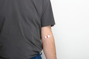 Blood donorship. Man in gray T-shirt hand taped with patch with red drop after giving blood on gray...