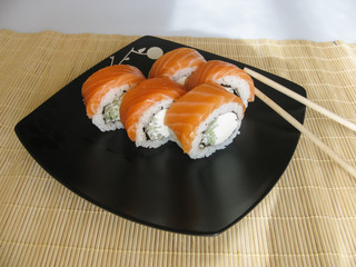 Philadelphia rolls on a black plate with chopsticks