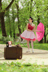 Retro style photo. A girl in a pink dress and hairstyle in the style of the 40-50s holds a pink...