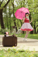 Retro style photo. A girl in a pink dress and hairstyle in the style of the 40-50s holds a pink...