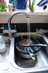 Obraz premium A running tap fills dirty pans with water so that they can soak in a kitchen sink to make them easier to clean.