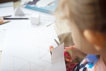 Child's hands cut paper with scissors. Child making geometric shapes. Home education.