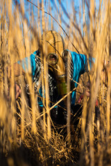 Man in blue t shirt and scarf Shemagh in gas mask sneaky sitting and spying in reeds field. Environmental protection of ecology. Concept of infection, apocalypse and pollution. Hope concept.