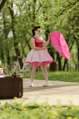 Retro style photo. A girl in a pink dress and hairstyle in the style of the 40-50s holds a pink...