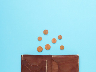 brown wallet with with scattered dollar and euro coins on blue background. last money, poverty, unemployment, job loss, saving concept. Flat lay, copyspace