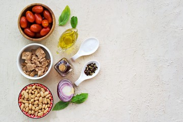 Prepared salad ingredients with canned tuna, white beans and tomato on a light concrete background. Italian food. Salad recipes. Copyspace, top view.