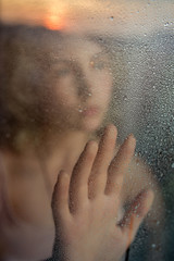 Silhouette of a girl behind a glass with raindrops. Reflection of sunset in the glass. Conceptual photography: the theme of loneliness,self-isolation, fencing off.