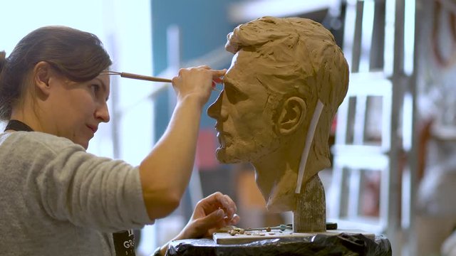 Woman sculptor at work. The process of preparing clay sculpture for molding and casting from plaster. Profession of restorer.