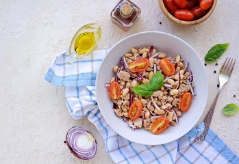 Traditional Italian salad with boiled beans, tomatoes, canned tuna and purple onions in a gray plate on a light concrete background. Dressed with olive oil. Italian food.