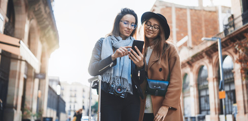 Girls plans trip on internet mobile phone, tourists using smartphone in europe city. Holiday friendship concept. Travelers hold cellphone, online technology