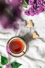 Top view of cup of black tea with cookies on the bed with lilac, flat lay. Breakfast concept.