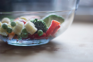 Frozen vegetables mixture with broccoli, red pepper, baby carrot, baby corn and peas in a glass bowl