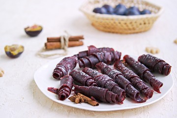 Pastille, handmade natural sweet apple and plum puree, rolled into rolls, on a white plate. Healthy desserts. Harvest apples and plums. Thanksgiving Day. Selective focus