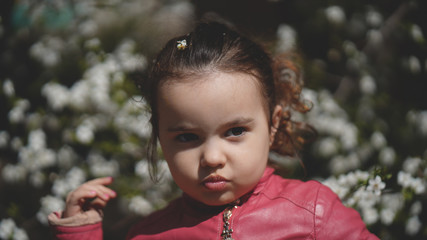 Portrait of cute little girl among the branches of blossoming tree in spring