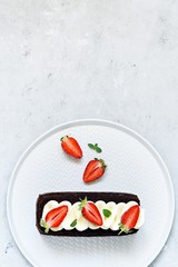 Chocolate brownie with airy vanilla cream and fresh strawberries. Chocolate cake with cream and fresh berries. Chocolate dessert on a plate.