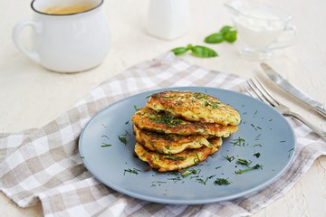 Fritters zucchini with feta cheese on a gray plate on a light concrete background. Served with sour cream. Zucchini recipes. Selective focus.